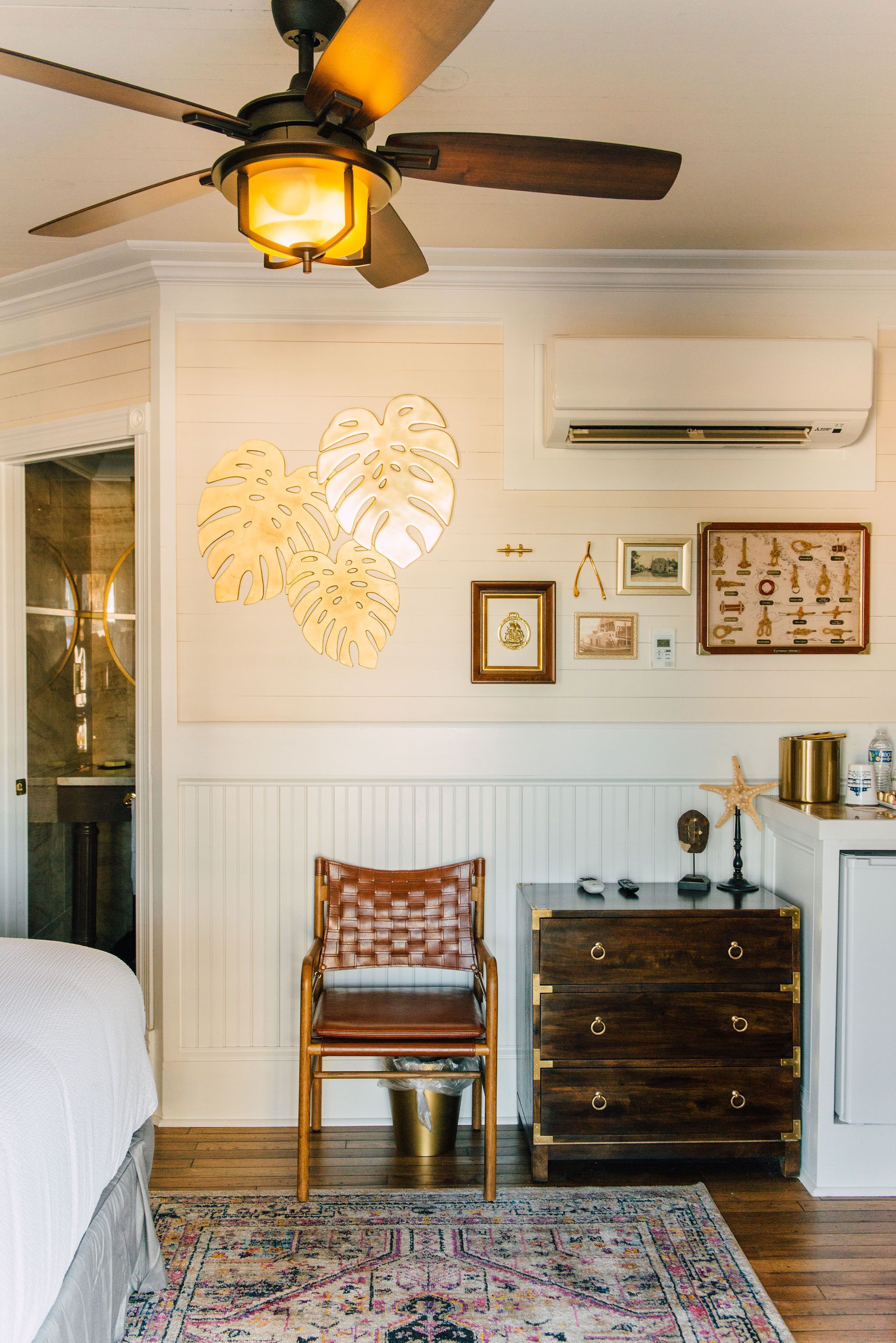 Un dormitorio con cama, una silla, cómoda, ventilador de techo y decoración en las paredes.