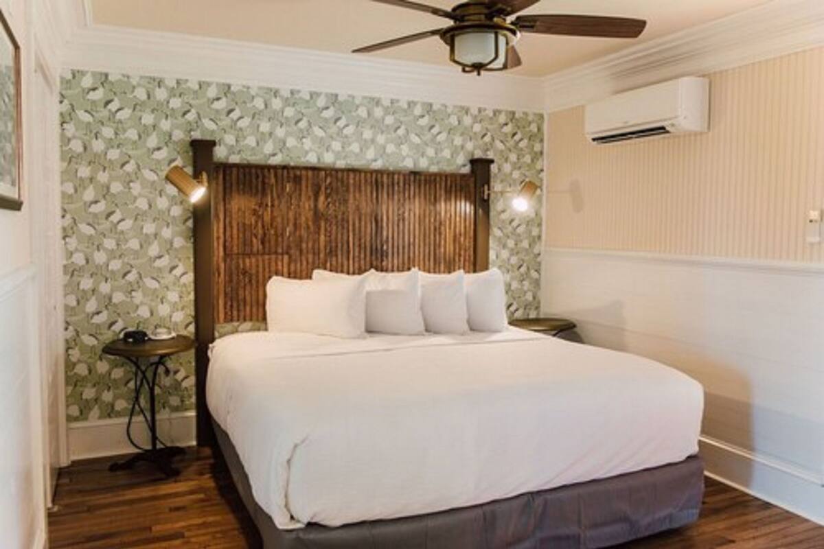 A bedroom with a wooden headboard, a bed with white bedding, a ceiling fan, and an air conditioning unit.