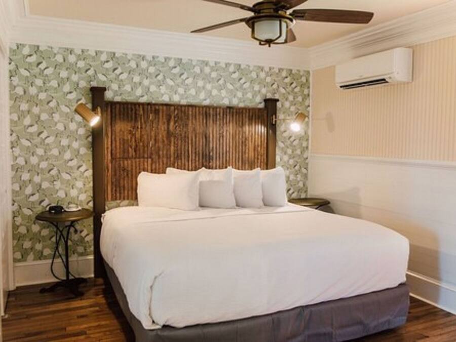 A bedroom with a wooden headboard, a bed with white bedding, a ceiling fan, and an air conditioning unit.