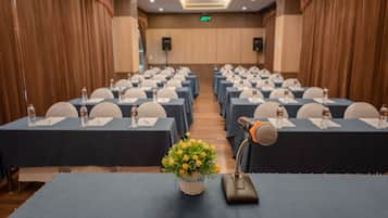 A conference room with rows of tables, each equipped with a microphone, water bottle, and notepad.