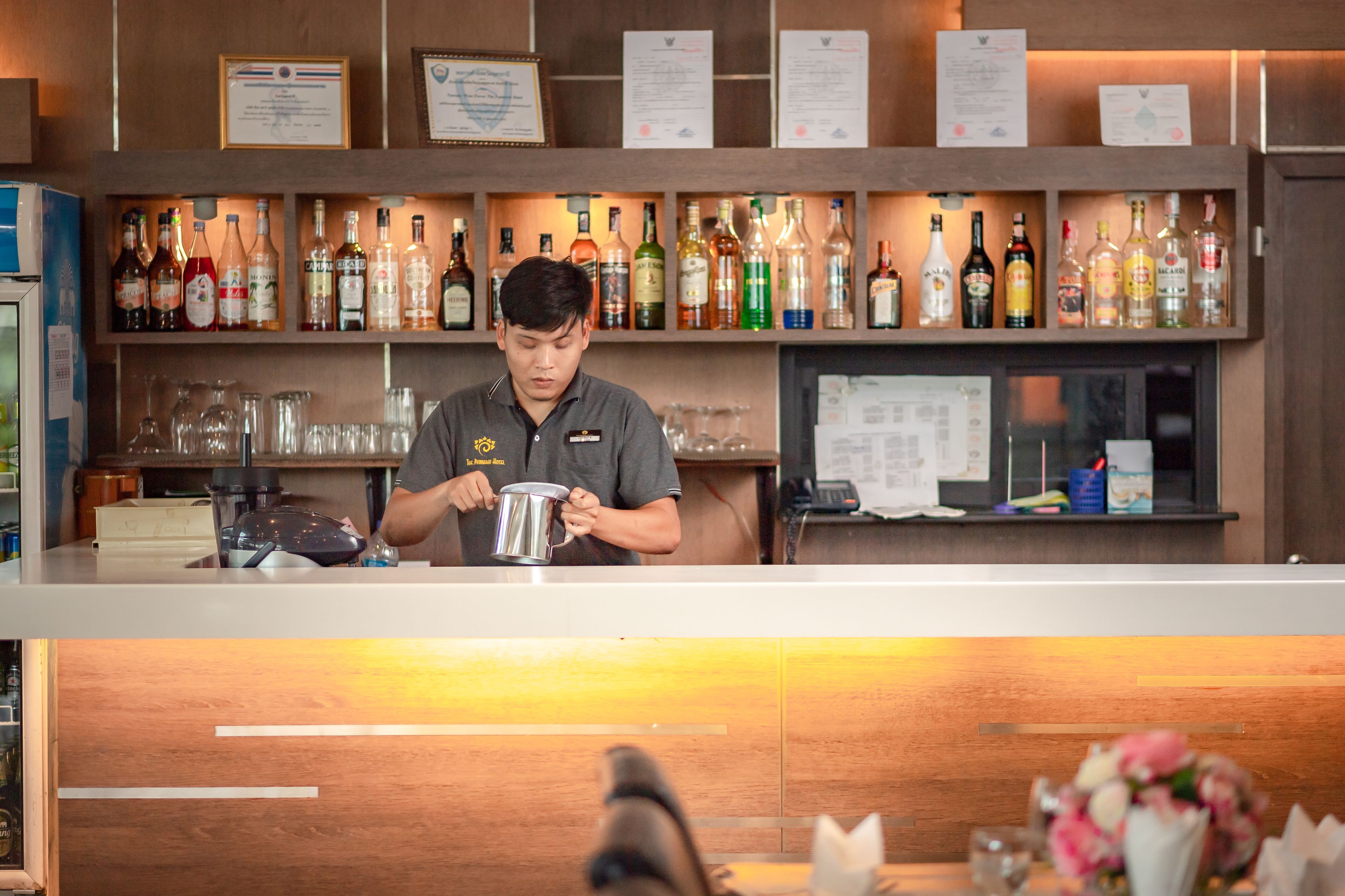 A bar area with a bartender preparing a drink, shelves with various liquor bottles, and a menu board.