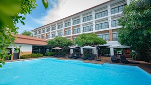 Un hotel con piscina, mobiliario exterior y un edificio grande de varios pisos.