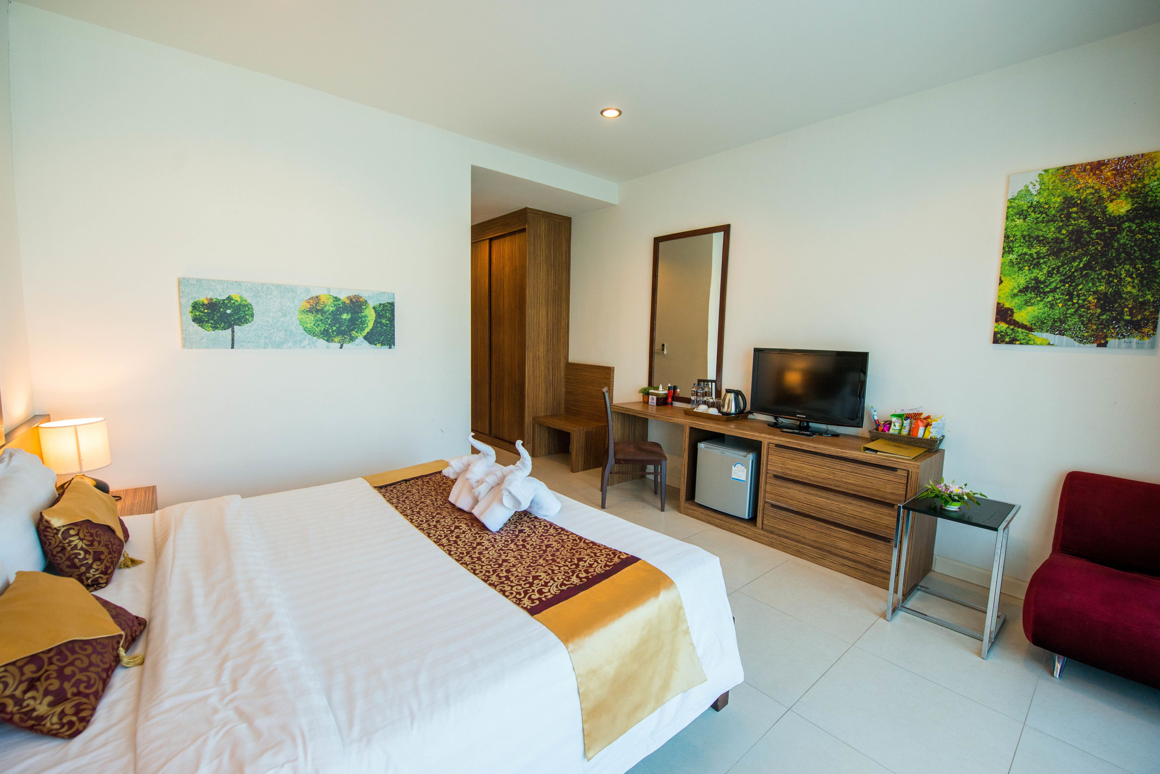 A hotel room with a bed, a desk, a television, and a red chair.
