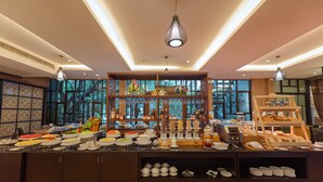 Zona de bufé con diferentes alimentos y bebidas, un expositor de pan escalonado y un aplique decorativo colgante.