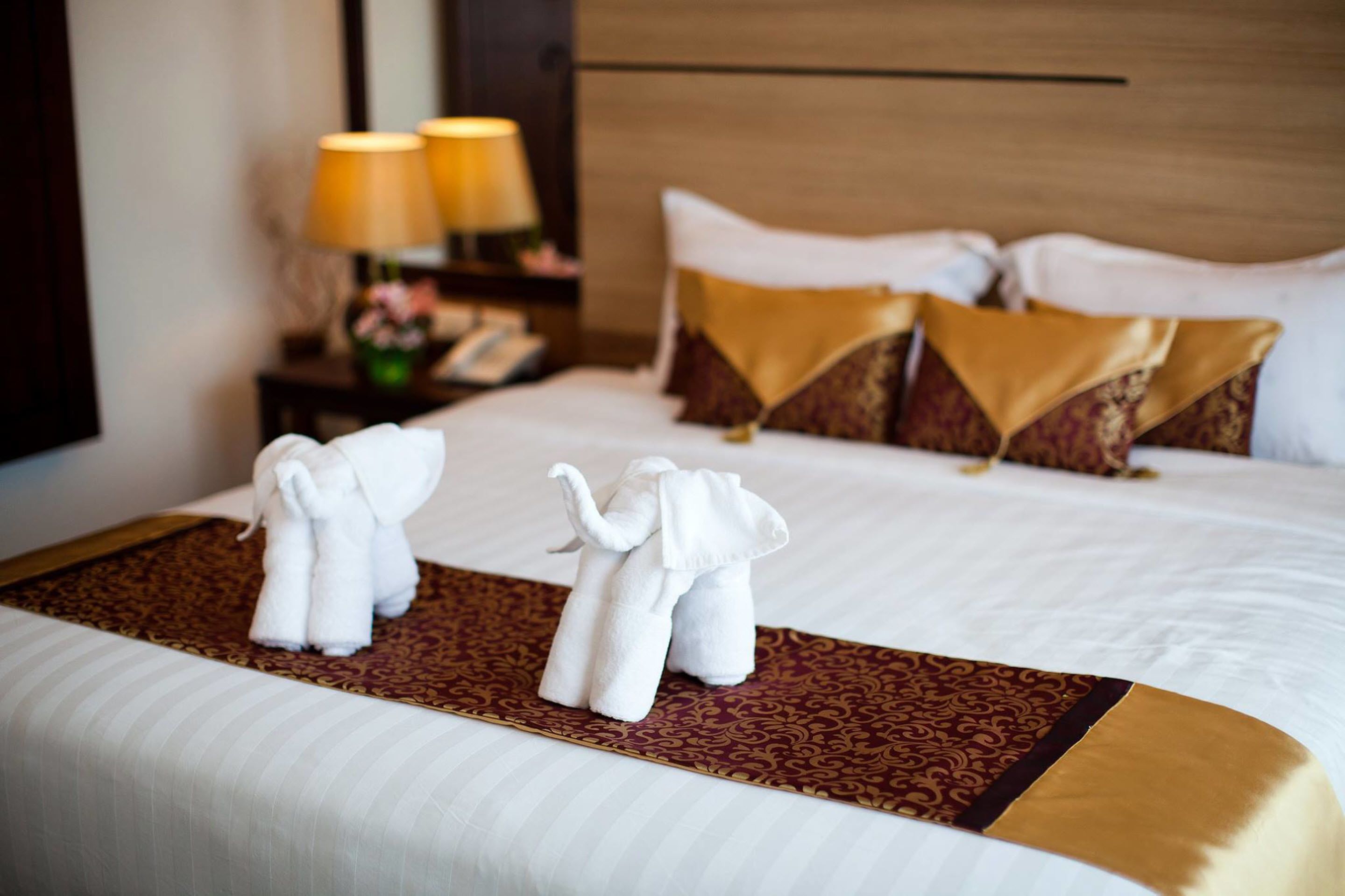 Habitación de hotel con una cama bien hecha, dos lámparas en una mesita de noche y un cojín decorativo.