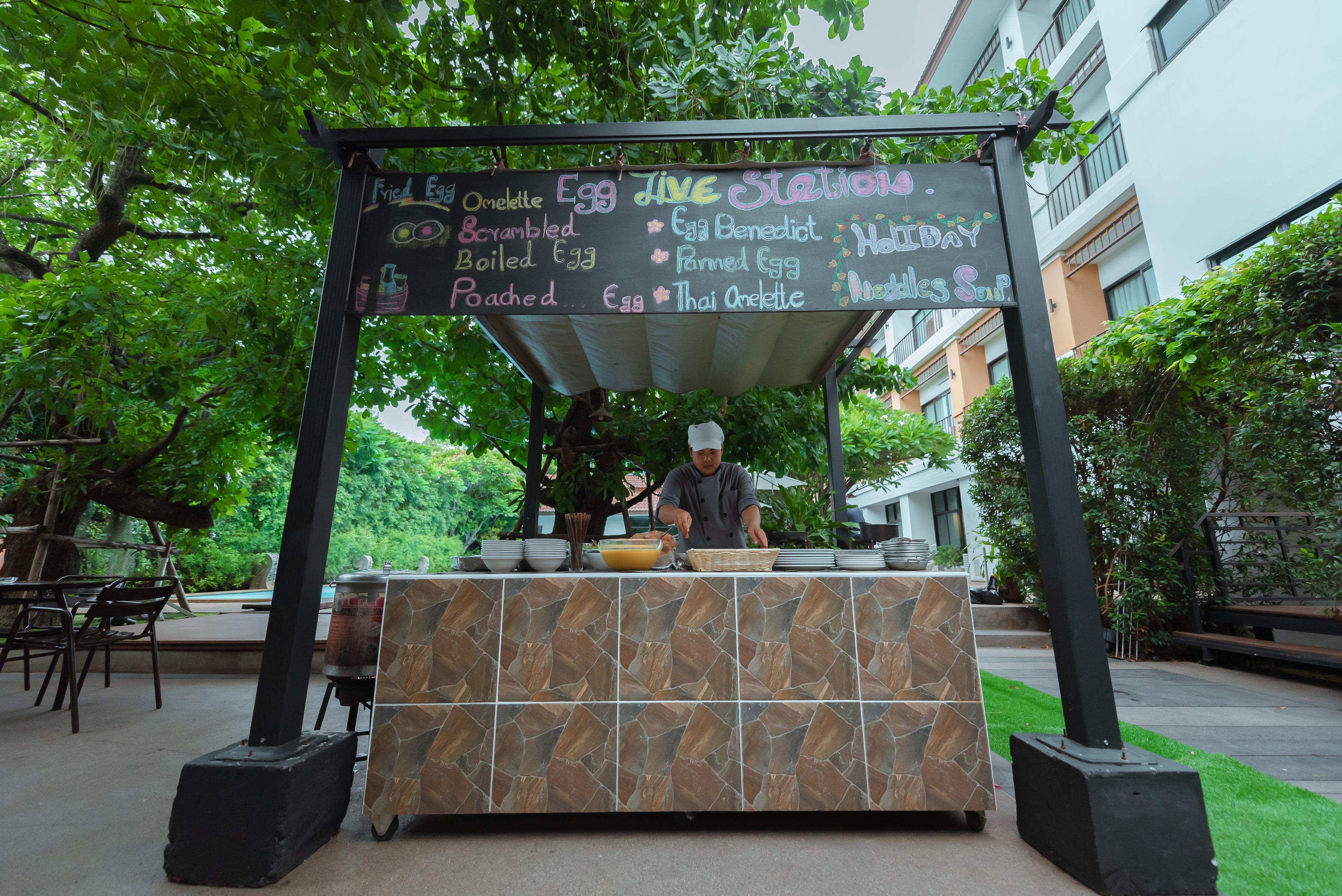 Un puesto de comida con un cartel de menú que muestra diferentes platillos de huevo y un cocinero preparando alimentos.