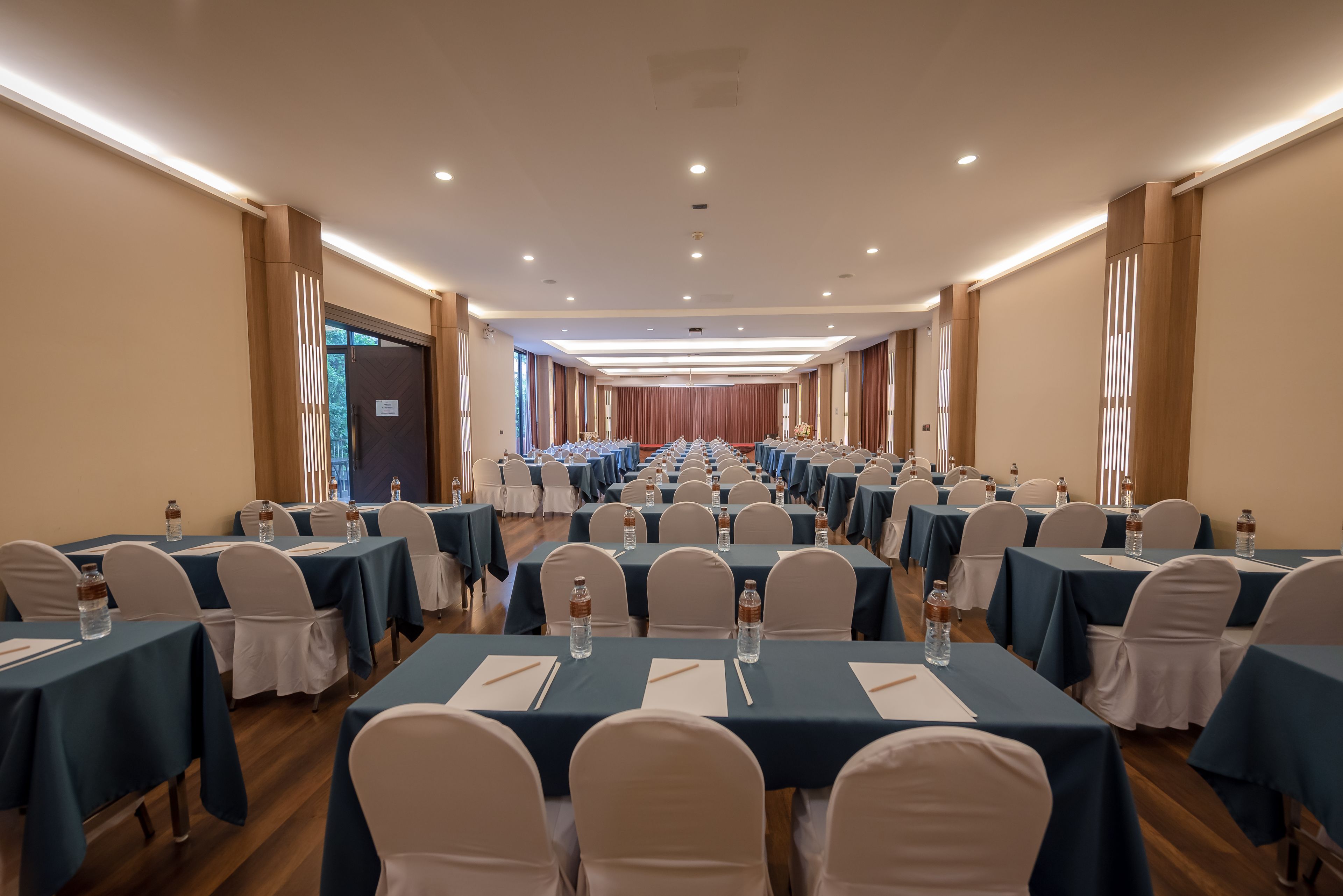 A conference room with rows of tables and chairs, equipped with water bottles and notepads.