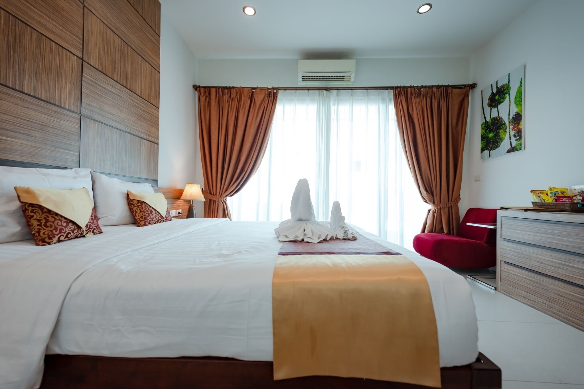 A hotel room with a large bed, a red chair, a wooden headboard, and a wall-mounted air conditioner.