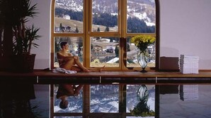 Ein Wellnessraum mit einem großen Bogenfenster, das einen Blick auf eine verschneite Berglandschaft bietet.