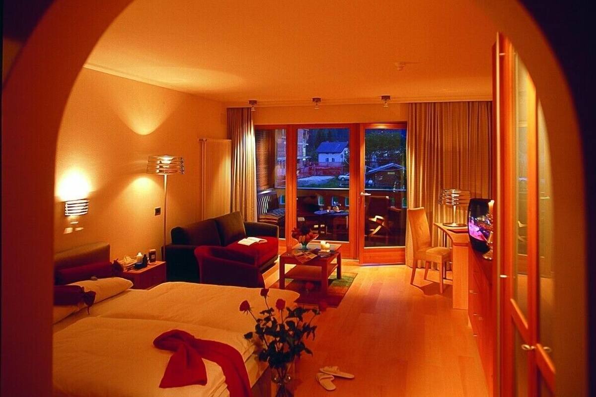 A hotel room with a large bed, a sofa, a desk, and a view through a glass door.
