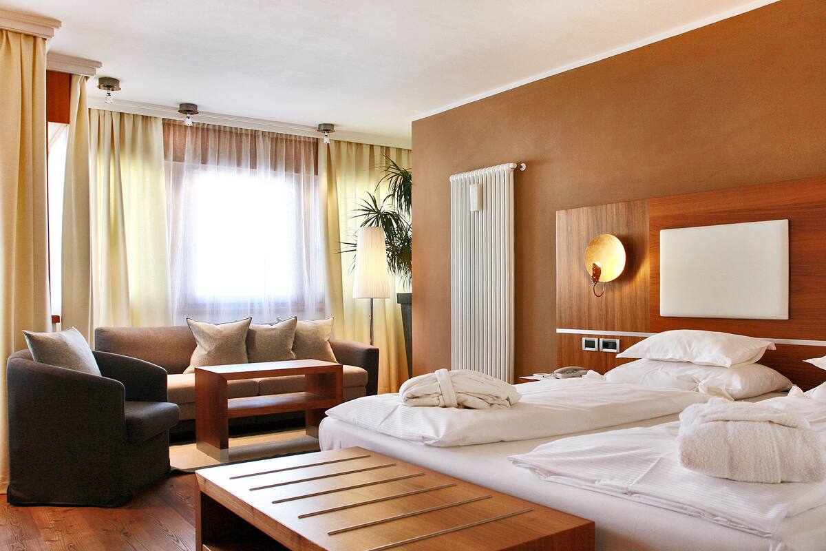 A hotel room with a bed, a sofa, a wooden table, and a desk.