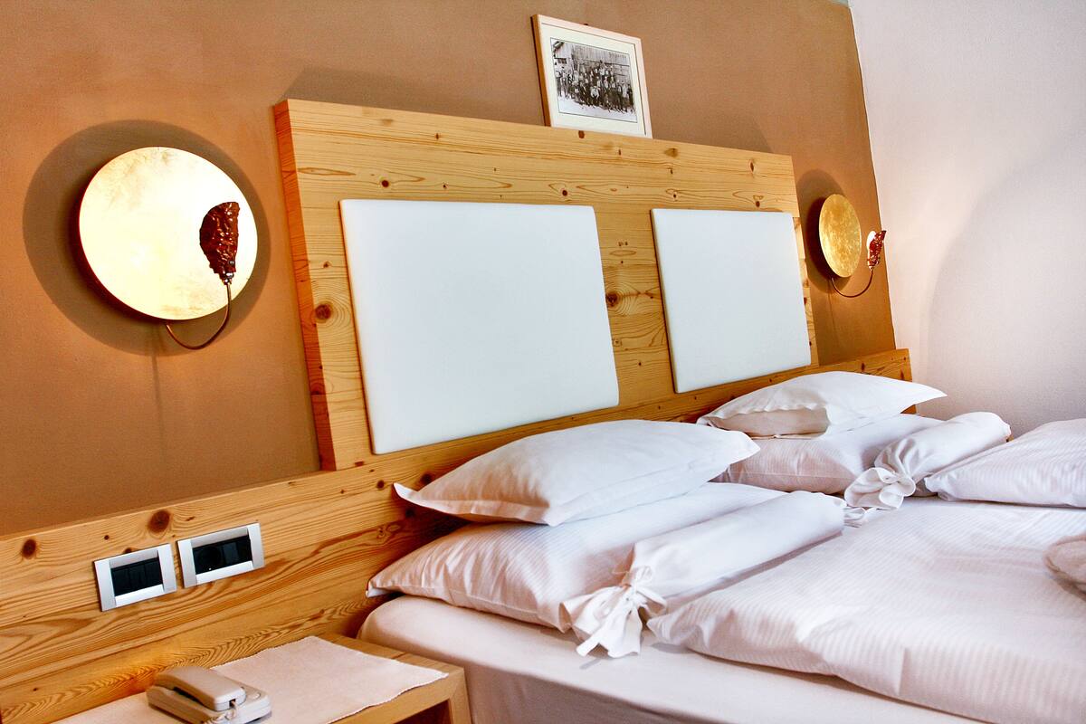 A hotel room with a wooden headboard, two bedside tables, a bed with white linens, and wall-mounted lamps.