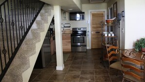A kitchen with a staircase, stainless steel appliances, wooden cabinets, and a dining area with chairs and a table.