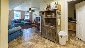 A living room with a sofa, a dining table, and a kitchen area with cabinets and a trash can.