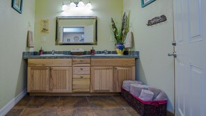 Un baño con tocador de madera, un espejo, un lavamanos y piso de baldosas.