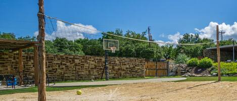 An outdoor basketball court with a wooden fence, a stone wall, and a basketball hoop.