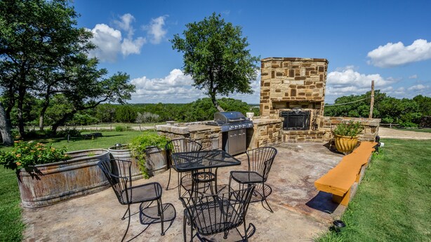An outdoor patio with stone barbecue grill, metal chairs, and a stone fireplace.