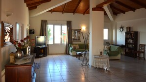 A spacious living room with a high ceiling, a television, a sofa, a coffee table, and a bookshelf.