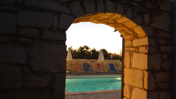 A stone archway leading to a pool area with lounge chairs and umbrellas.