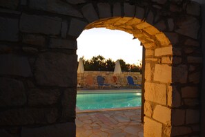A stone archway leading to a pool area with lounge chairs and umbrellas. - Villa Galini (Hersonissos)