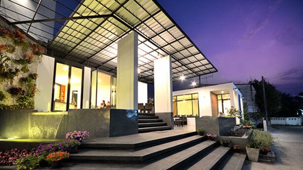 A modern building with a glass facade, outdoor seating area, and steps leading to the entrance. - Good Home Udonthani (Udon Thani)