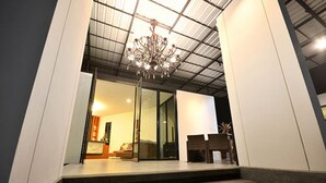 A modern interior with a staircase leading to a living area, a chandelier, and a glass door entrance. - Good Home Udonthani (Udon Thani)