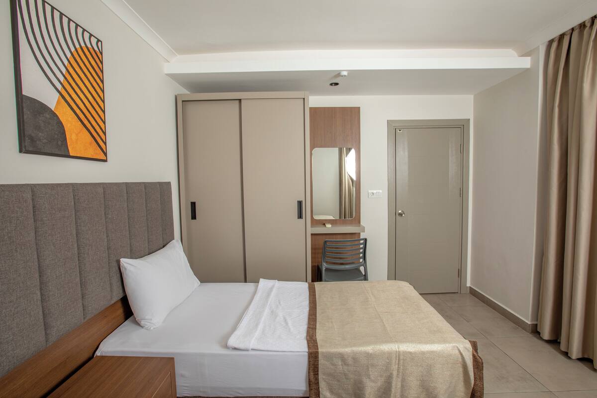Hotellihuone, jossa on sänky, vaatekaappi, työpöytä ja peili.