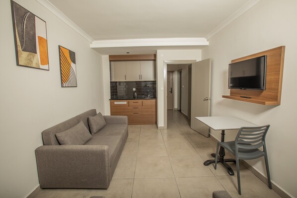 A modern living room with a sofa, a TV mounted on the wall, and a kitchen in the background.