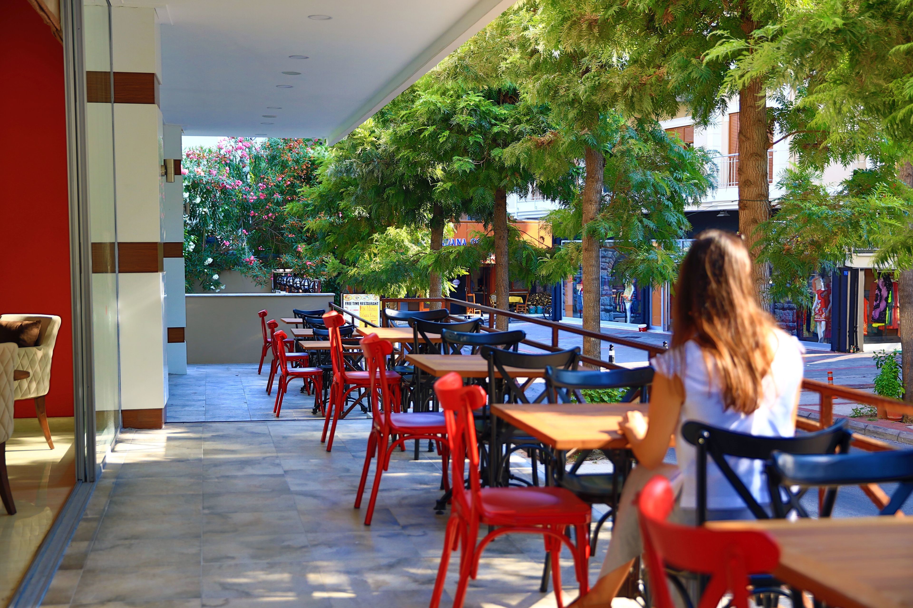 An outdoor café with tables and chairs, surrounded by trees and buildings.