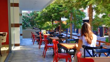 An outdoor café with tables and chairs, surrounded by trees and buildings.