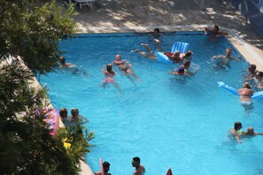 Una piscina con gente disfrutando del agua, rodeada de árboles y un cielo despejado.
