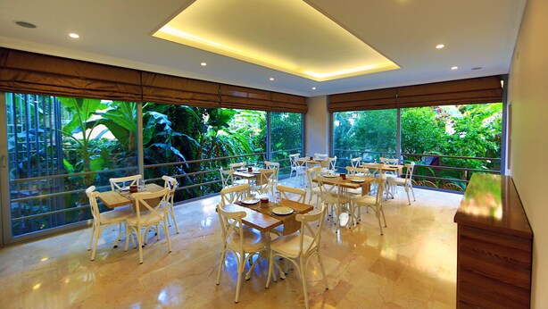 Un vaste espace dédié à la salle à manger, avec de nombreuses tables et chaises, de grandes fenêtres offrant une vue sur une végétation luxuriante et un design de plafond moderne.