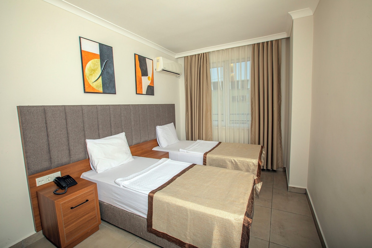 A hotel room with two beds, a bedside telephone, and artwork on the wall.