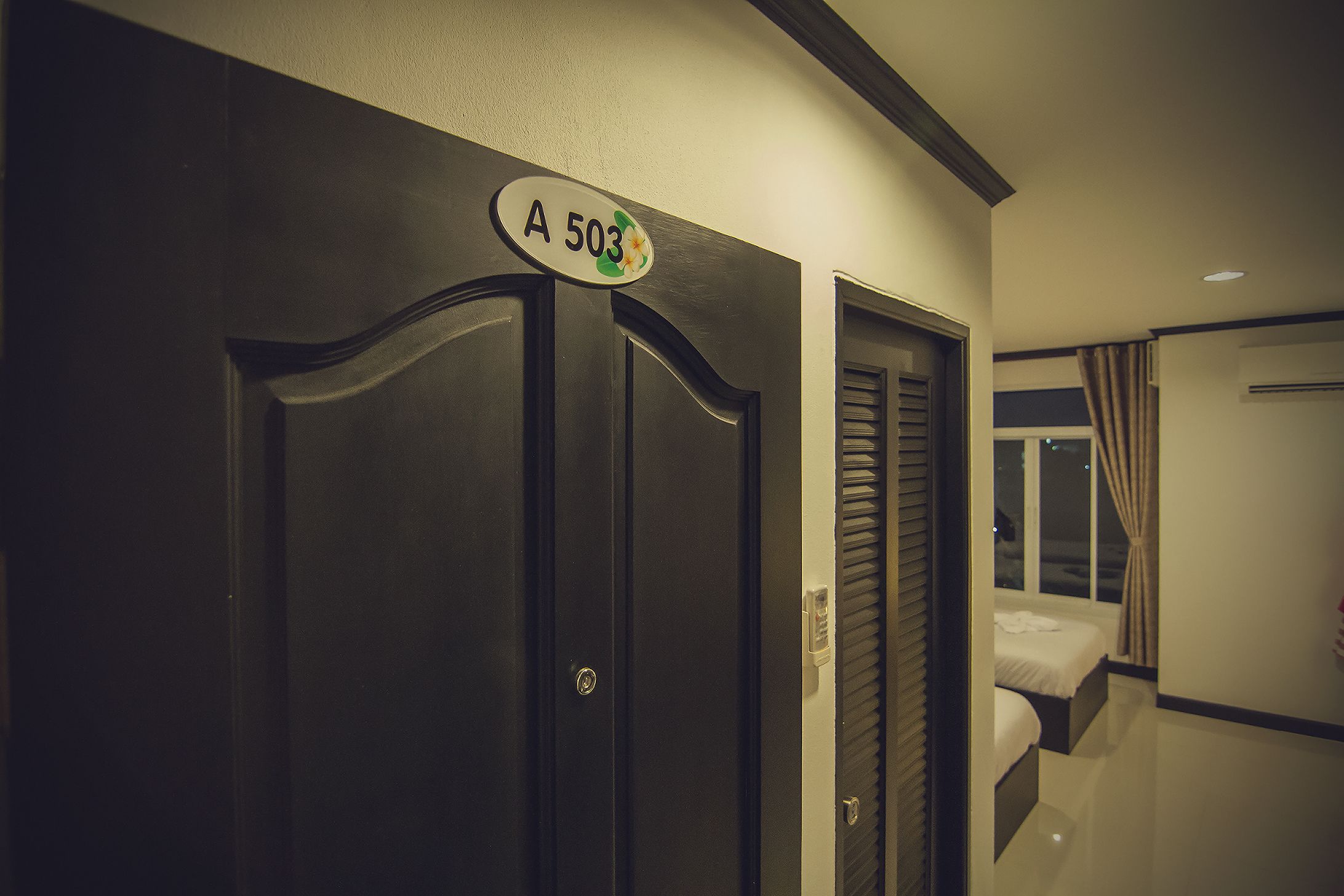 Une chambre d’hôtel avec une porte en bois sombre, une enseigne au-dessus et une fenêtre avec des rideaux.