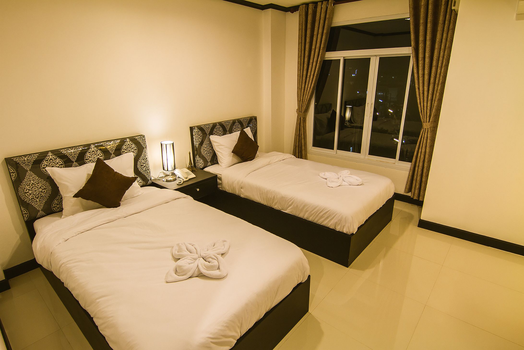 A hotel room with two beds, each with a headboard, a nightstand, and a lamp.