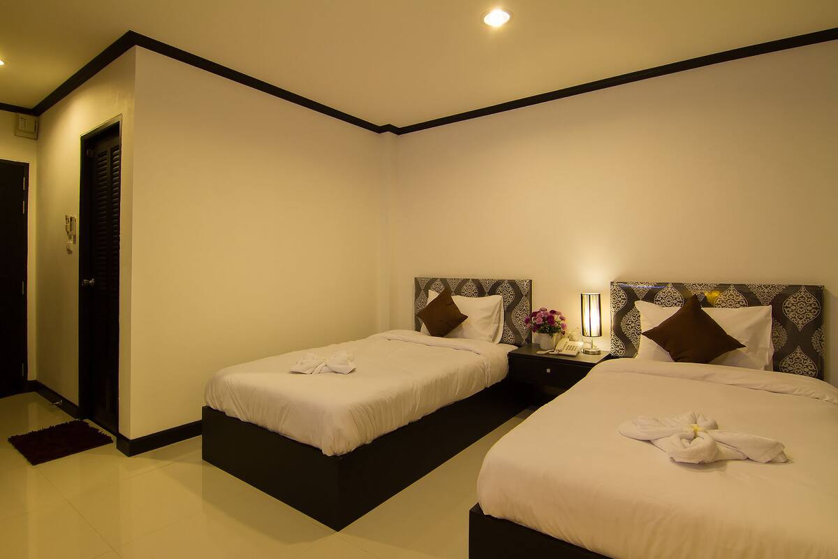 A hotel room with two beds, a nightstand with a lamp, and a door.