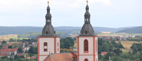 A church with two towers and a red roof, surrounded by a rural landscape.