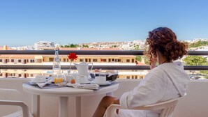 Een balkon met een ontbijttafel, met uitzicht op een stadsbeeld met gebouwen en een heldere lucht.