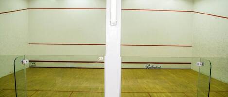 A squash court with glass walls and a wooden floor, marked with red lines.