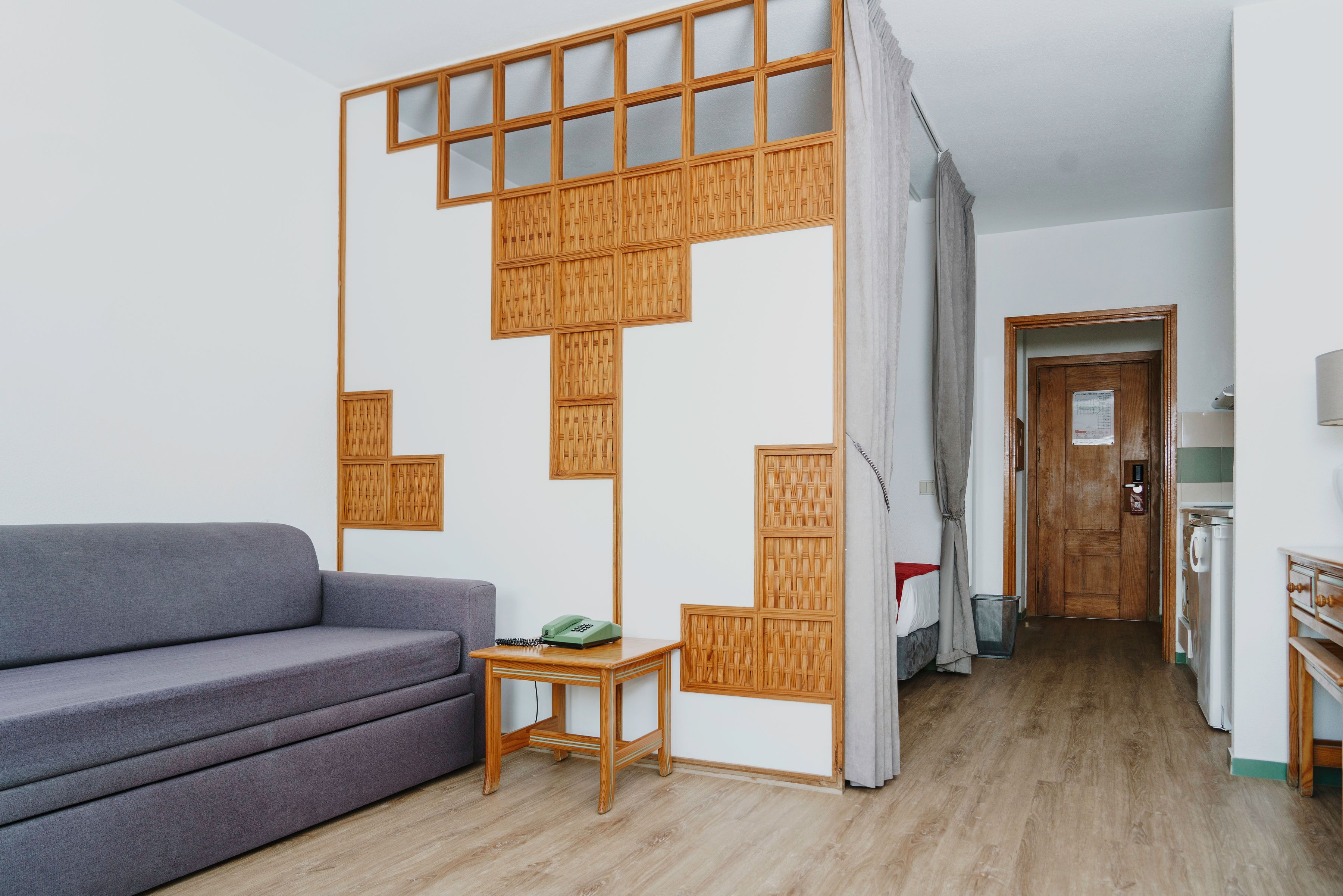 Una sala moderna con un sofá gris, una mesita de madera pequeña y una cocina al fondo.