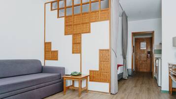 Una sala moderna con un sofá gris, una mesita de madera pequeña y una cocina al fondo.