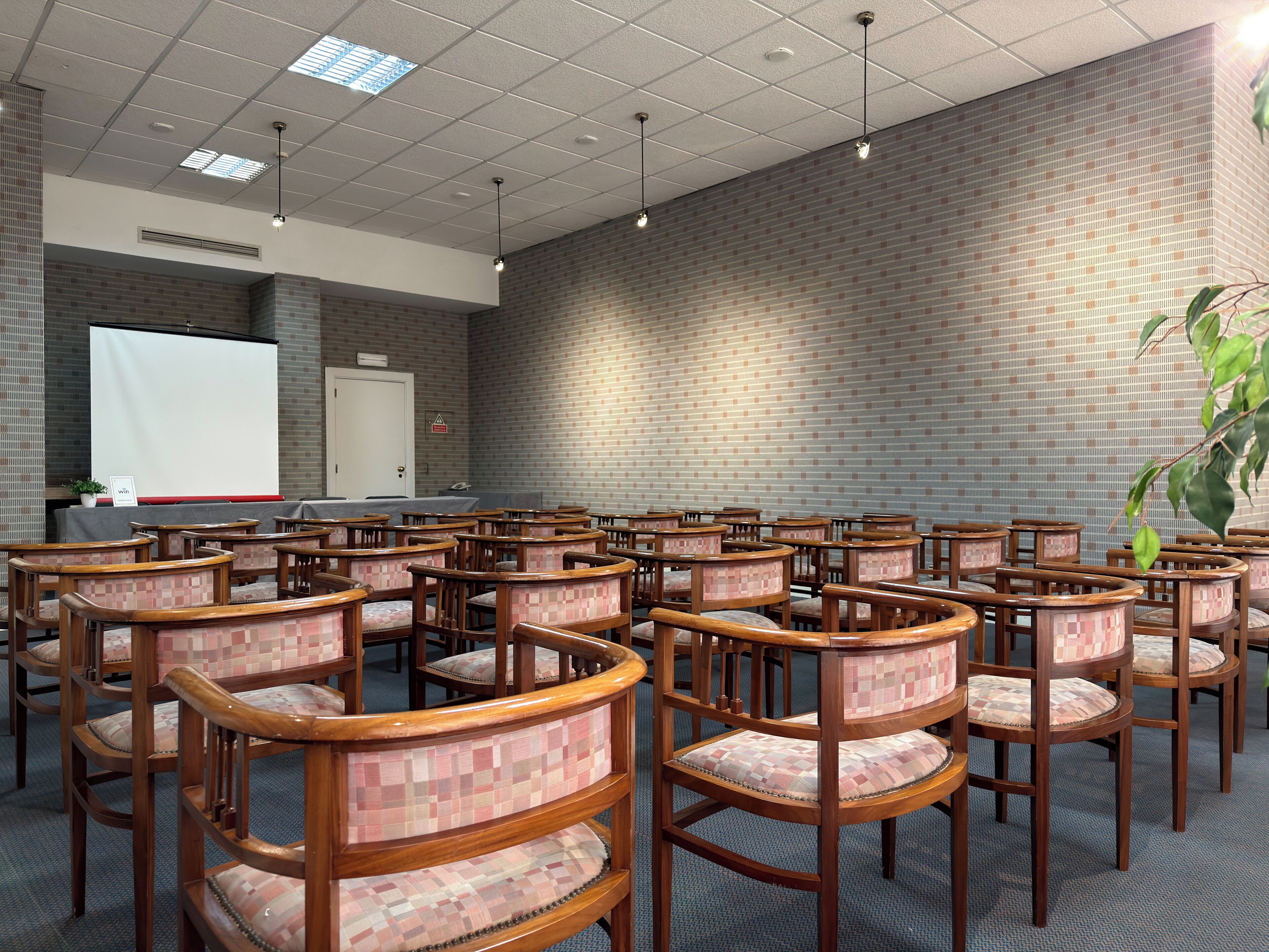 A conference room with multiple wooden chairs and a projector screen.