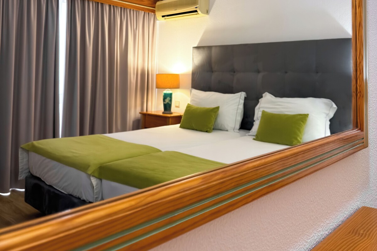 Ein Hotelzimmer mit Bett, Nachttisch, Lampe, Klimaanlage und einem großen Spiegel.