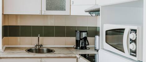 Una cocina con armarios blancos, un lavamanos de acero inoxidable, un microondas y una cafetera.