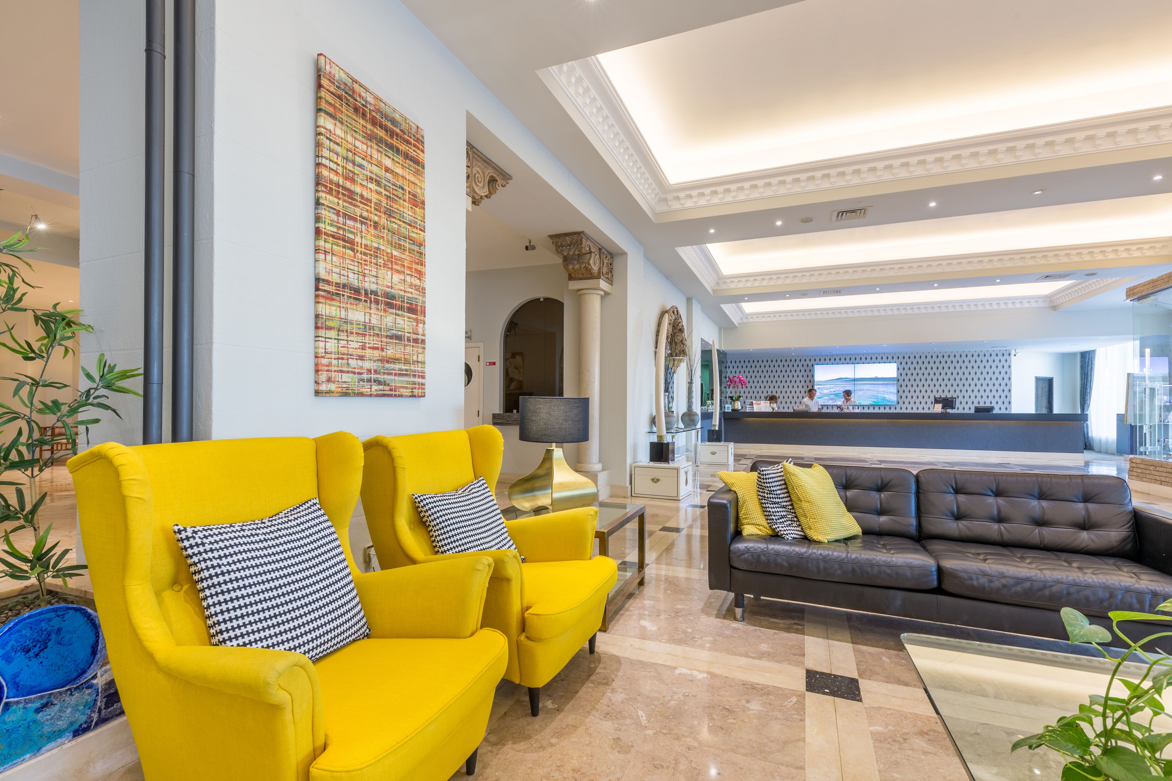 A modern hotel lobby with yellow armchairs, a grey sofa, and a reception desk.