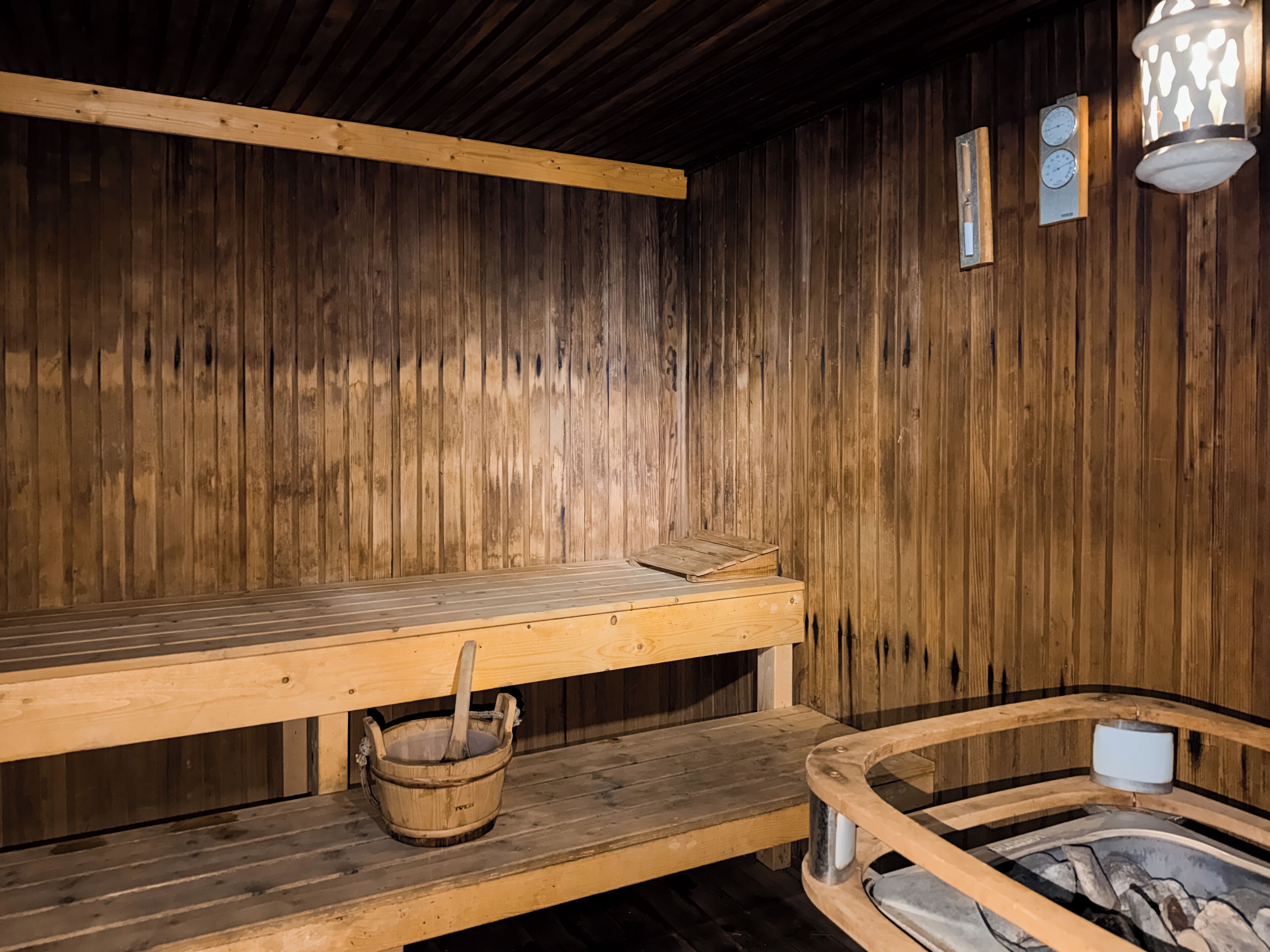 A sauna room with wooden benches, a wooden bucket, and a stone basin.