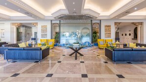 Een ruime lobby met een centraal glazen partitionering, twee banken, een ronde tafel en gele stoelen.