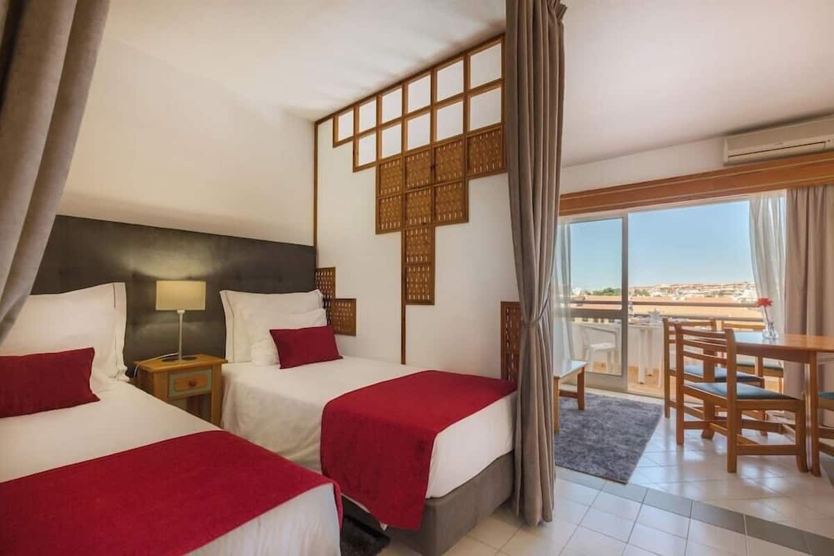 A hotel room with two beds, a balcony with a table and chairs, and a view of the city.