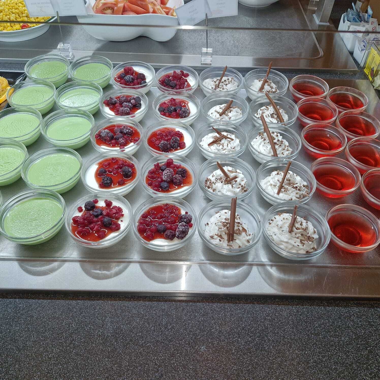 A buffet with various dishes including green and red sauces, desserts with berries and whipped cream, and a selection of corn and tomatoes.