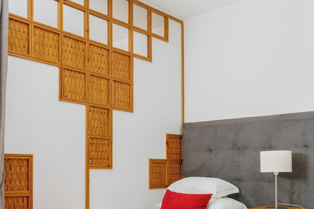 A hotel room with two beds, a grey headboard, a wooden wall panel, and a bedside table with a lamp.